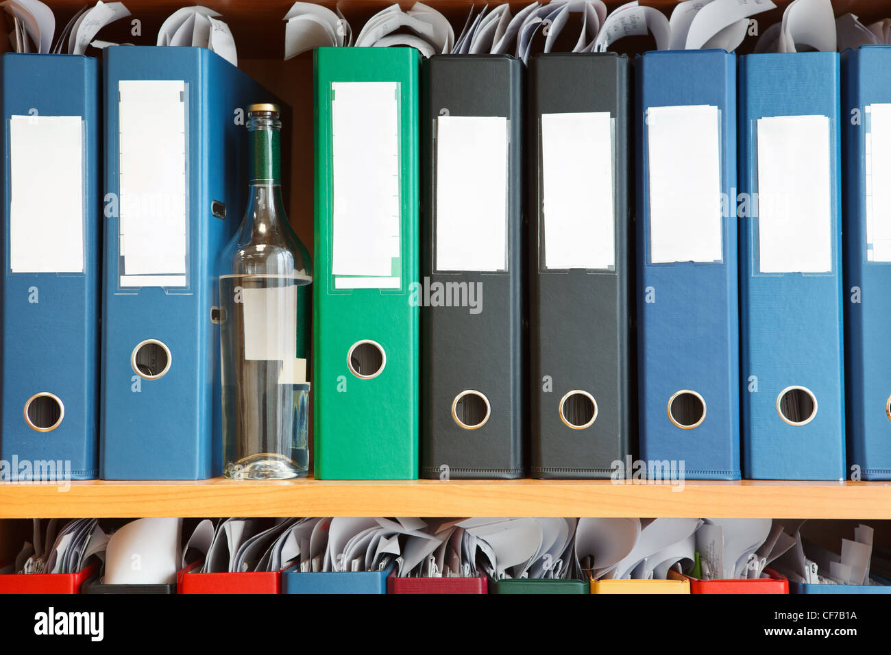 Glass bottle with alcohol hidden between file binders on shelves Stock Photo