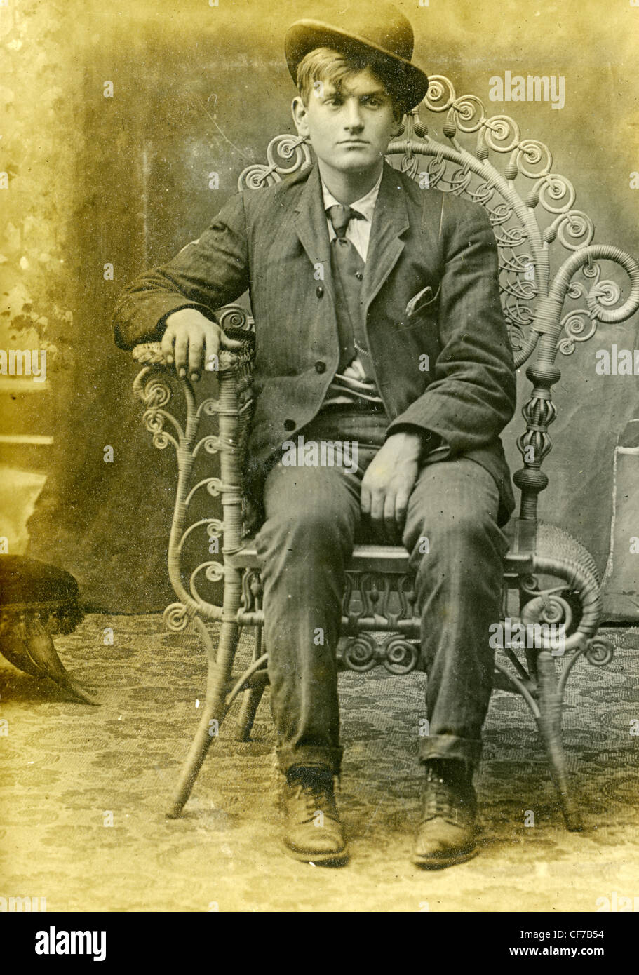 Boy sitting in chair wearing suit and bowler hat during late 1800s or ...
