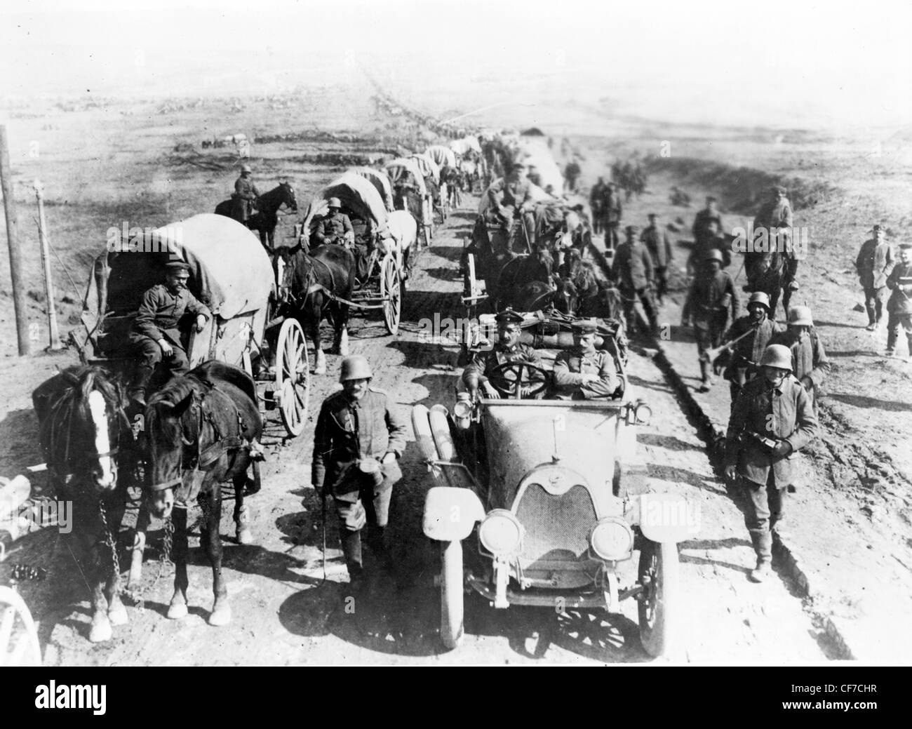 German officers in an automobile on the road with a convoy of wagons; soldiers walk along side the road, World War 1 Stock Photo