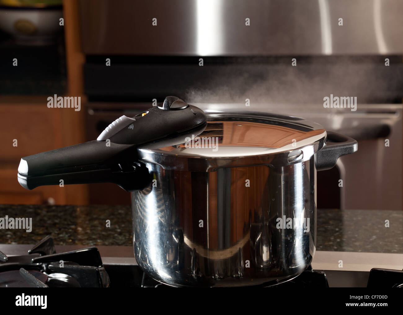 Steam escaping from lid of pressure cooker with reflection of modern kitchen Stock Photo