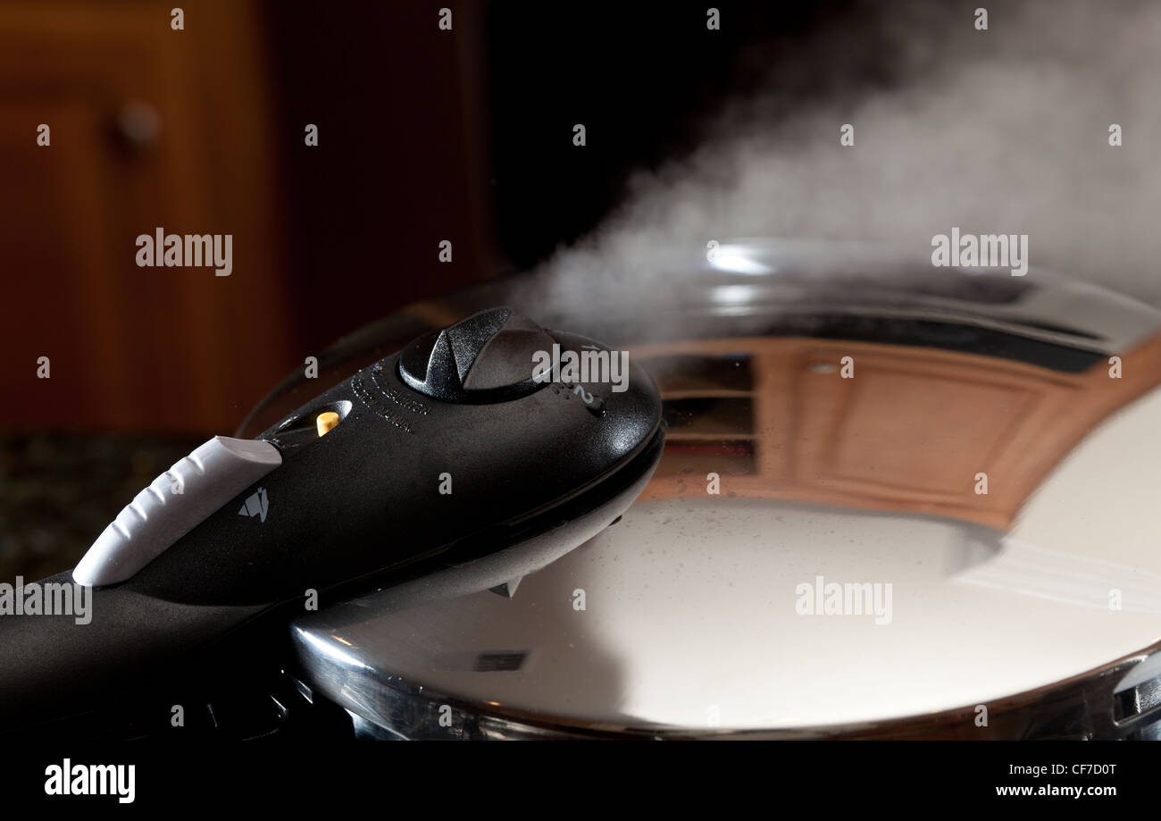 Steam escaping from lid of pressure cooker with reflection of modern kitchen Stock Photo