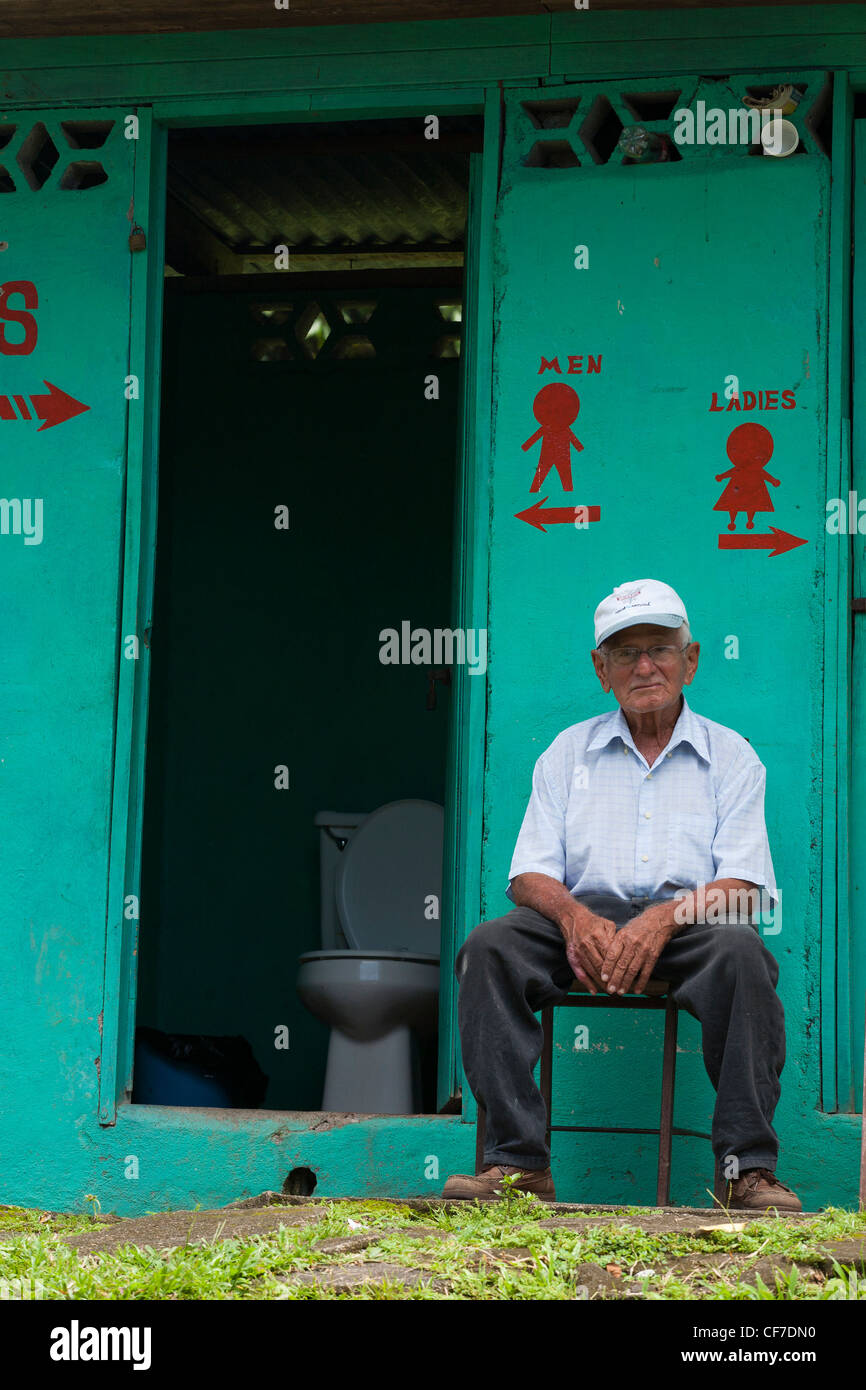 A Costa Rican attendent sits by the doors of the mens and woman's toilet in Puerto Viejo de Sarapiqui in Costa Rica Stock Photo