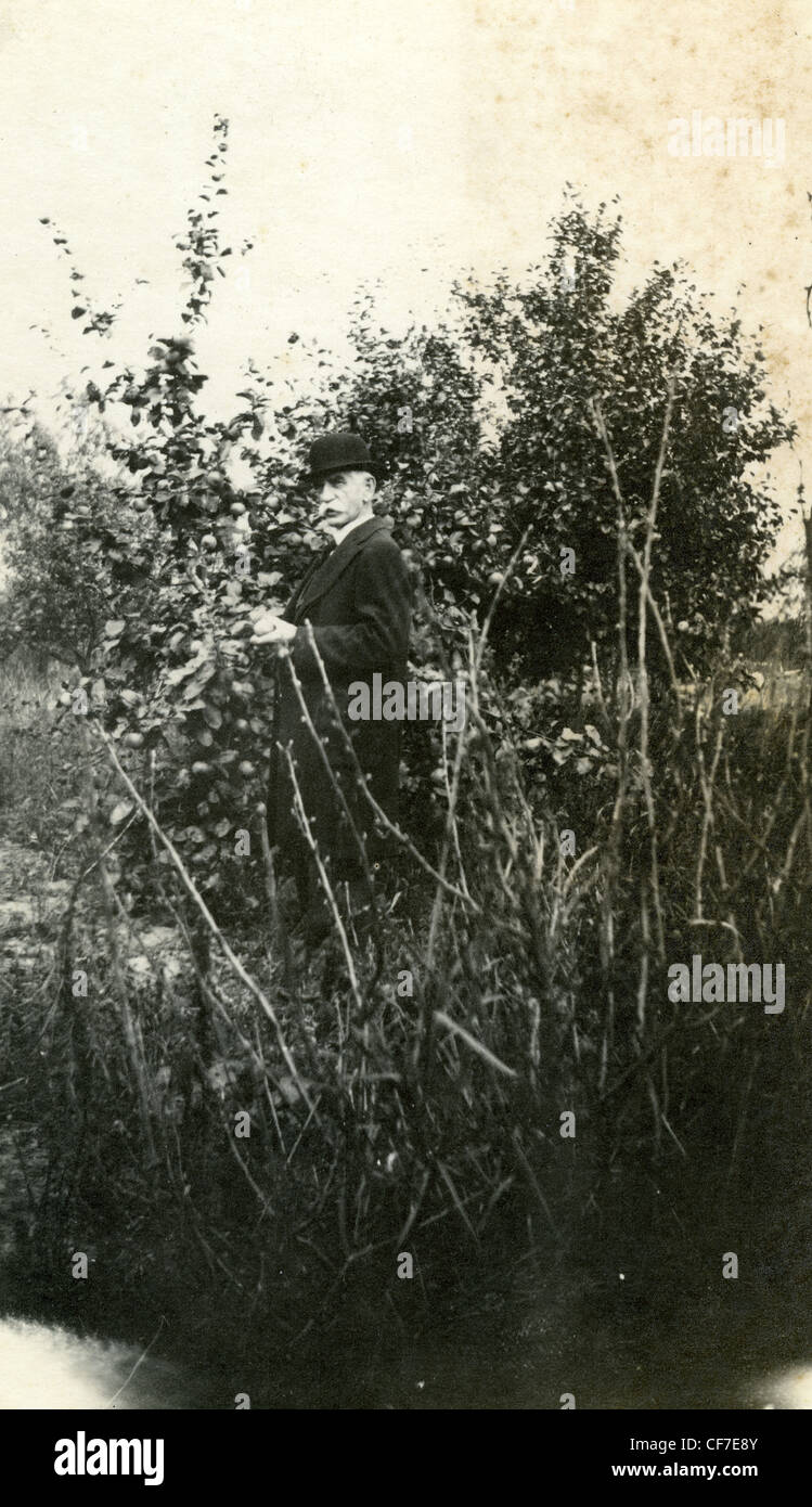 Fashionable man in bowler had holding fruit from tree black coat smoking pipe middle aged male 1900s 1800s rural farmer men's fa Stock Photo