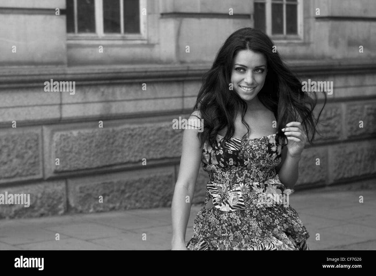 Female long black hair, wearing a floral patterned summer dress, walking on the street, smiling, looking to the side Cecilie Stock Photo