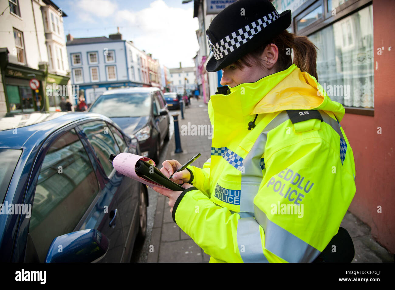A woman Dyfed-Powys police officer issuing parking ticket to a car parked on double yellow lines, Aberystwyth Wales UK Stock Photo