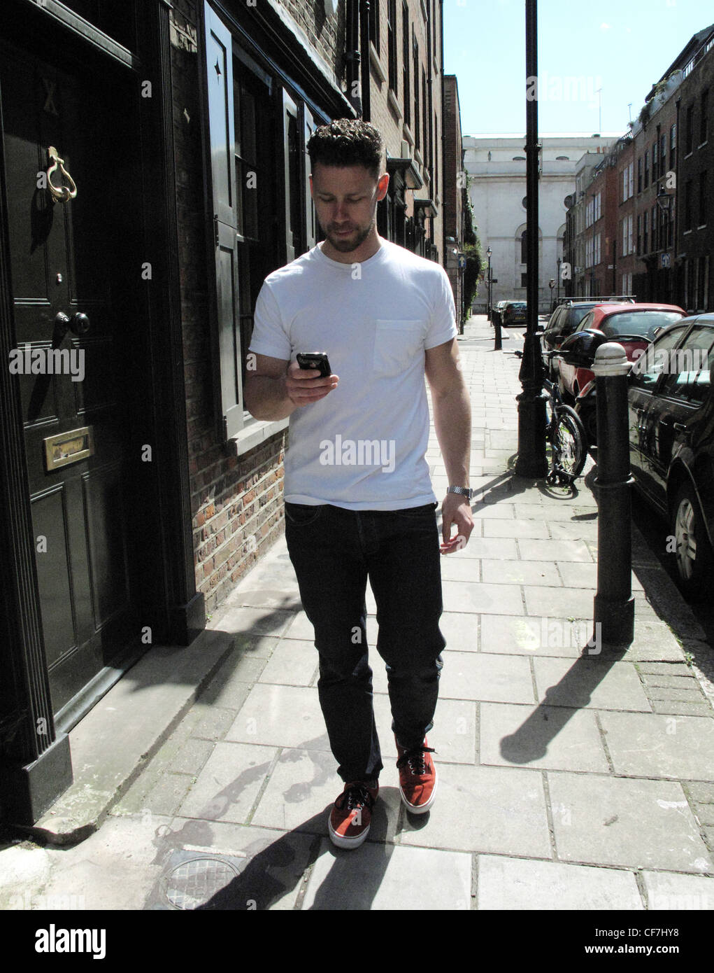Male with short brunette hair wearing a white t shirt, black jeans and red  trainers, walking down the street, using an i phone Stock Photo - Alamy
