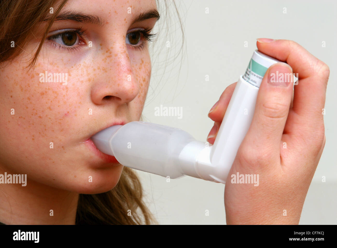A young female holding an inhaler attachedt to a plastic spacer devise to her face, to treat asthma Stock Photo