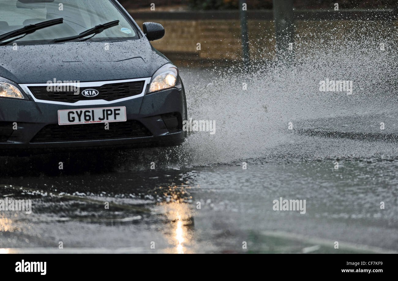 Car driving through heavy rain causing spray from surface water on road Stock Photo