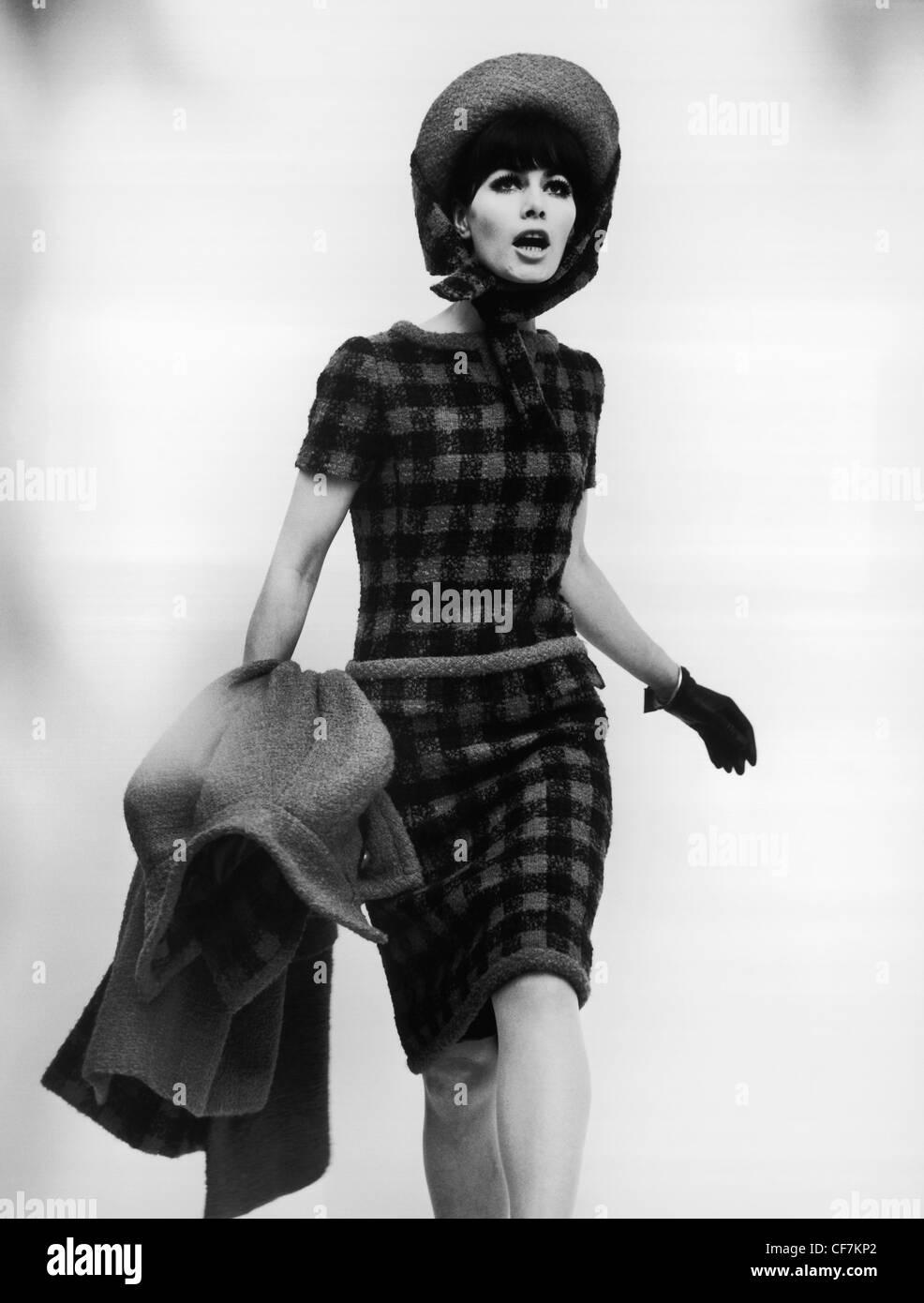 German Winter Fashions Female wearing checkerboard skirt suit, with hat, leather gloves, carrying tweed coat Gisela Them Stock Photo