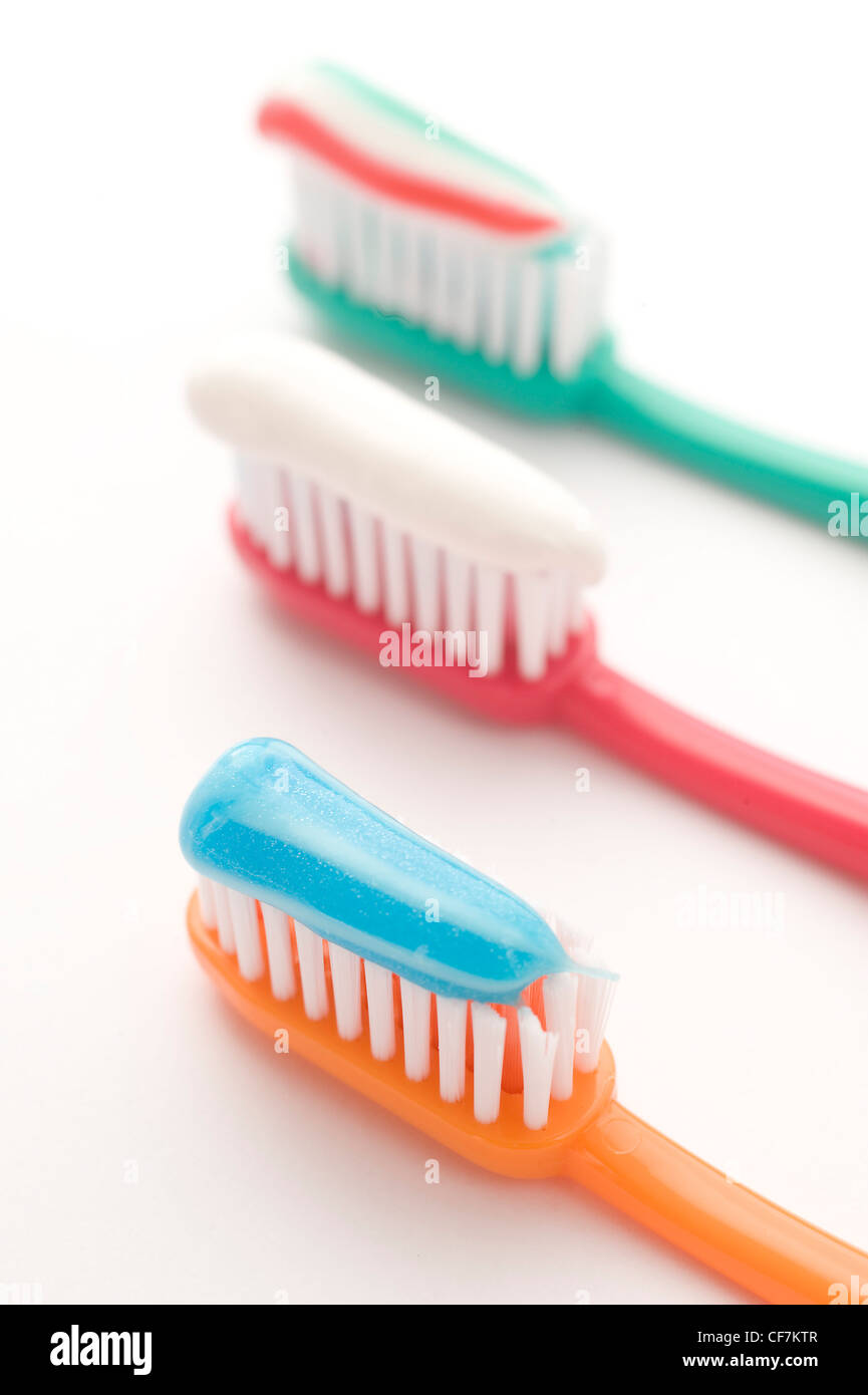 White and blue striped toothpaste on an orange toothbrush, white toothpaste on a red toothbrush