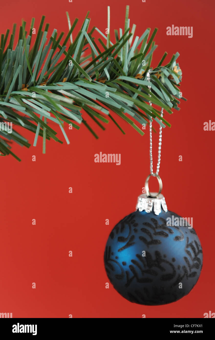 A dark blue and black patterned bauble hanging off the branch of a christmas tree, with a red background Stock Photo