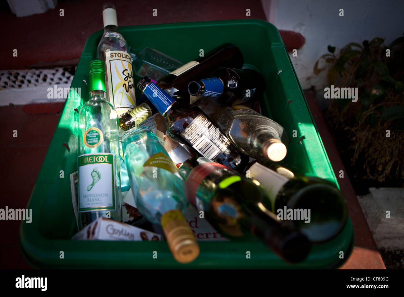 Empty wine, spirit and beer bottles in green recycling bin on doorstep