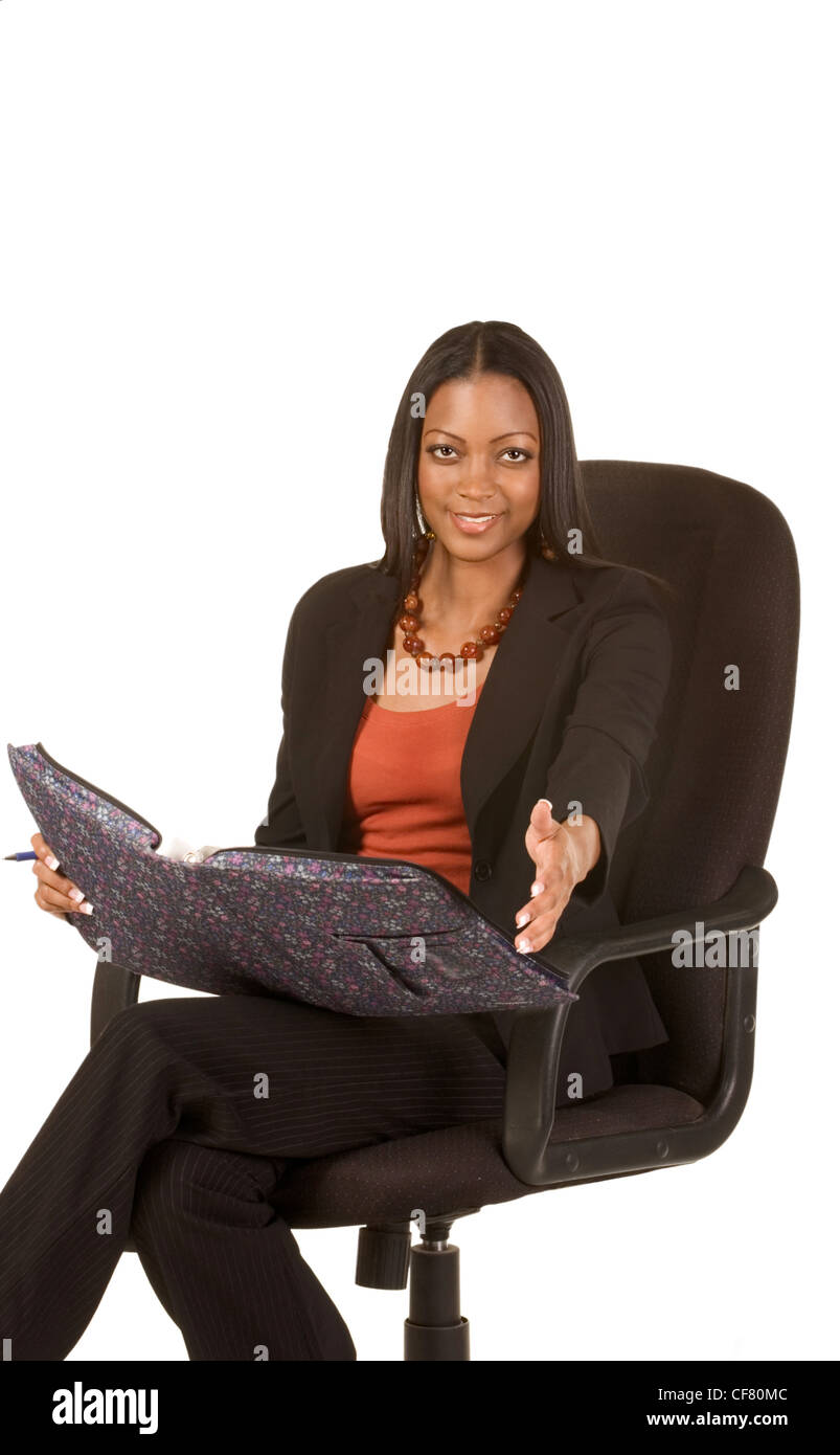 Young attractive ethnic woman in business suit sits in office chair with folder on her laps and stretches hand towards viewer Stock Photo