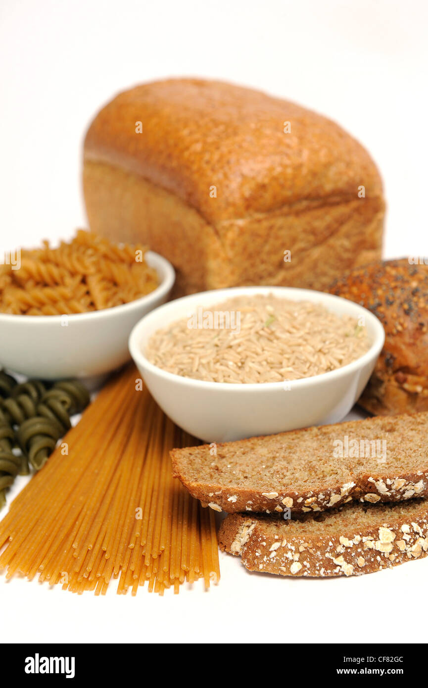 Two bowls filled long grain rice and dried fusilli pasta surrounded by loaves of bread, dried spaghetti and dried spinach Stock Photo