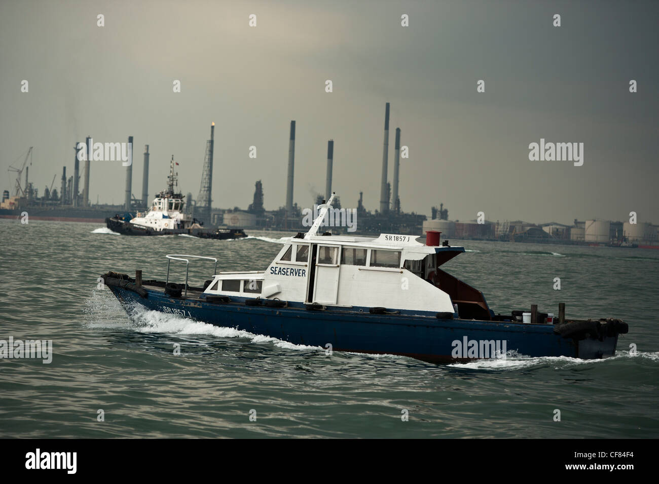 Small boats pass in front of an offshore oil refinery in Singapore Stock Photo