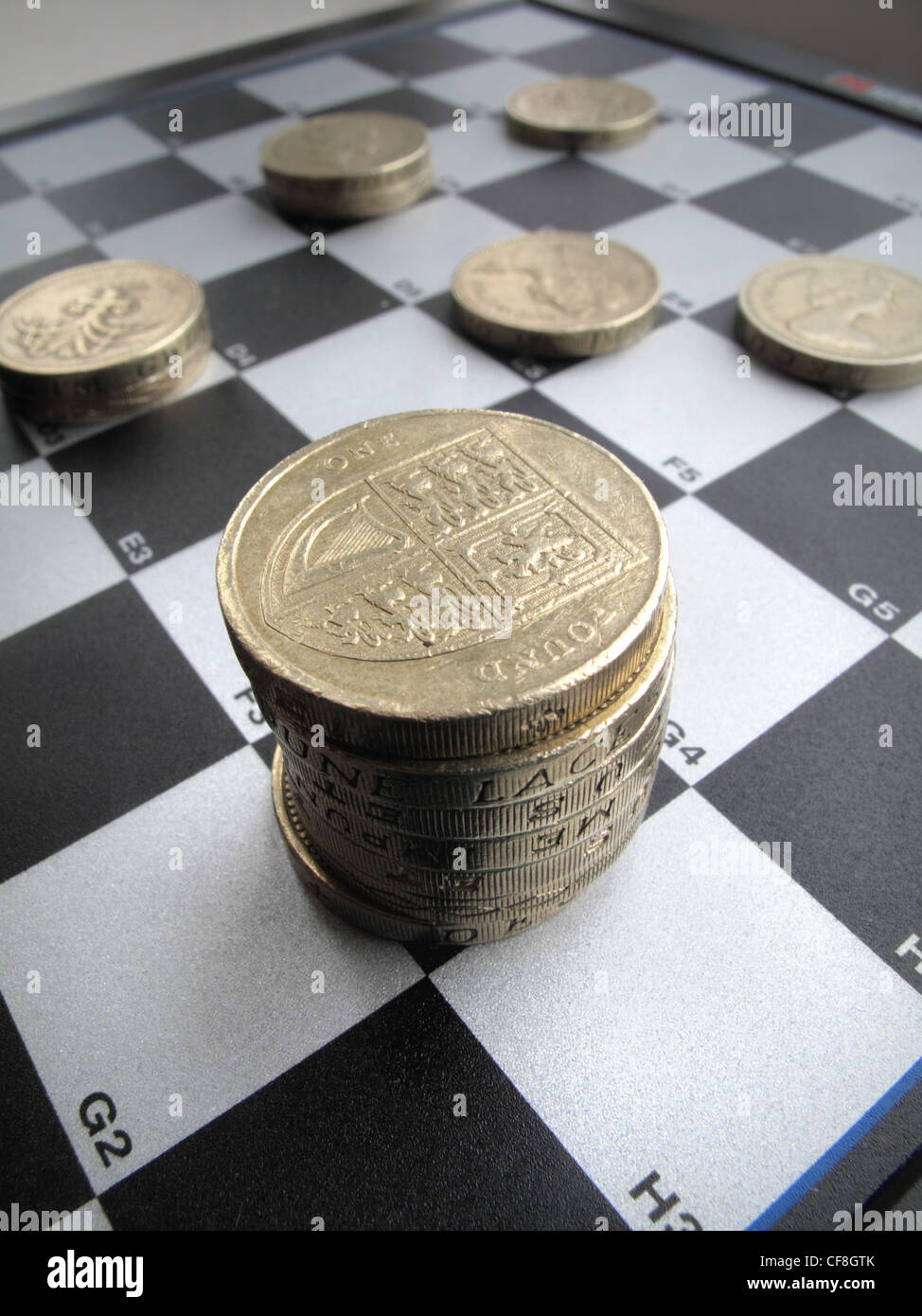 Stacked quantities of  British one  pound coins sit on a black and white checkers , chess game board. Stock Photo