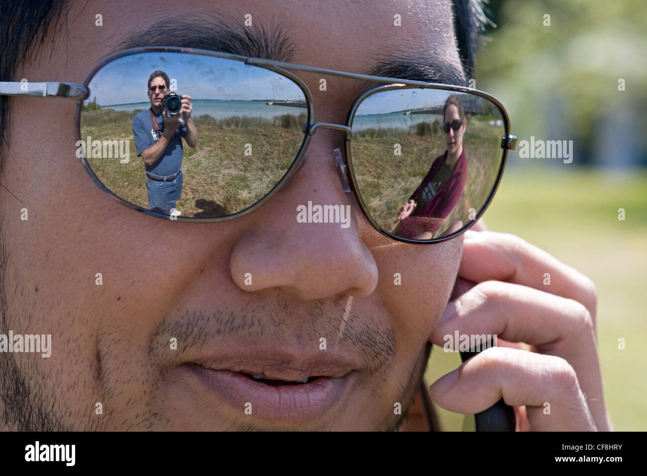 A man's wife and her father are reflected in his sunglasses while he talk on his cell phone. Stock Photo