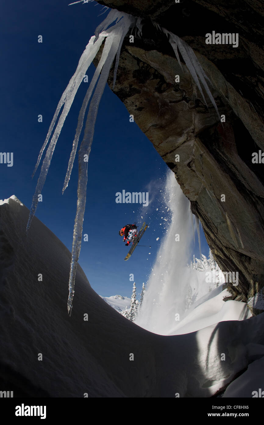 Freeskier jumping off cliff with icicles and snow cascading off rocks. Stock Photo