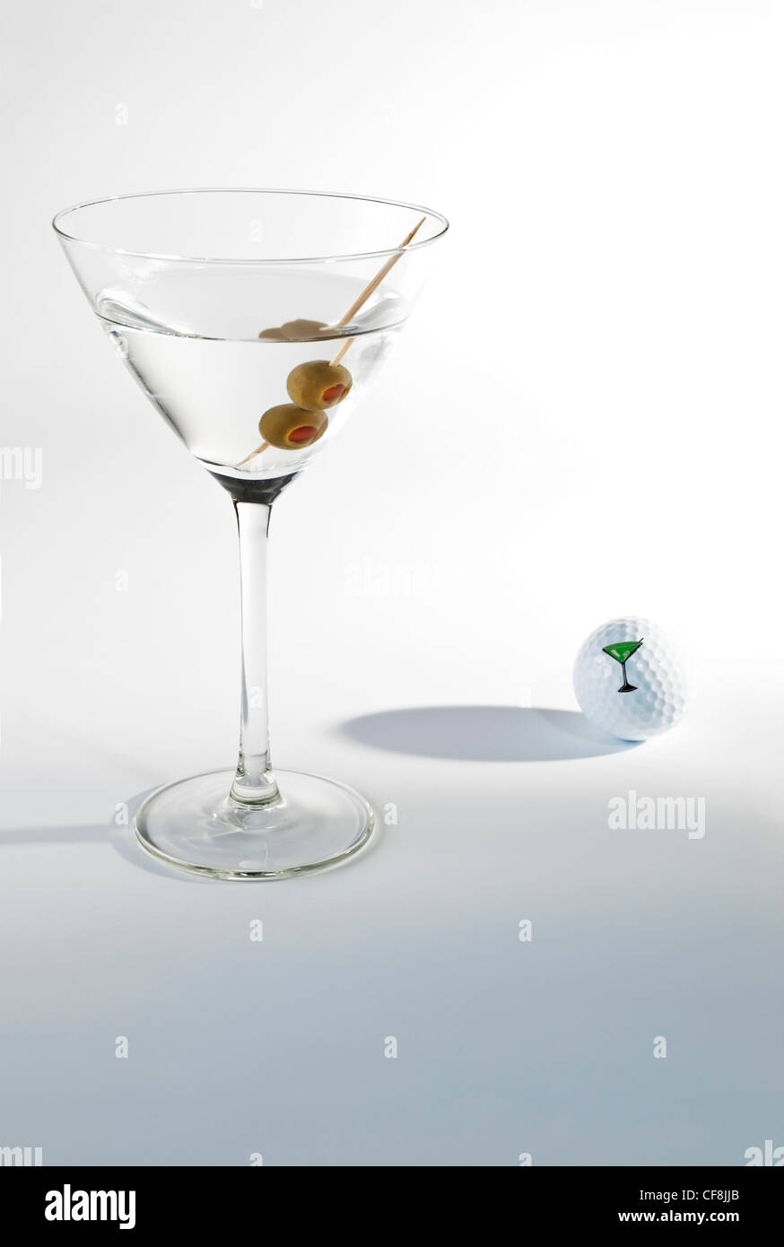 Martini with two olives on toothpick and a golf ball in background wit