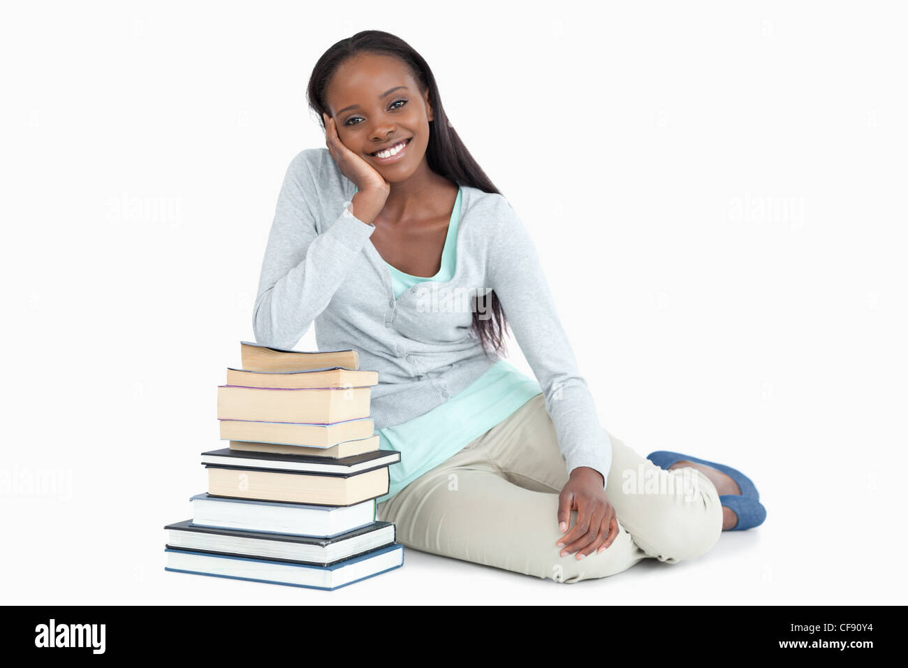 Smiling young woman leaning against a pile of books Stock Photo - Alamy