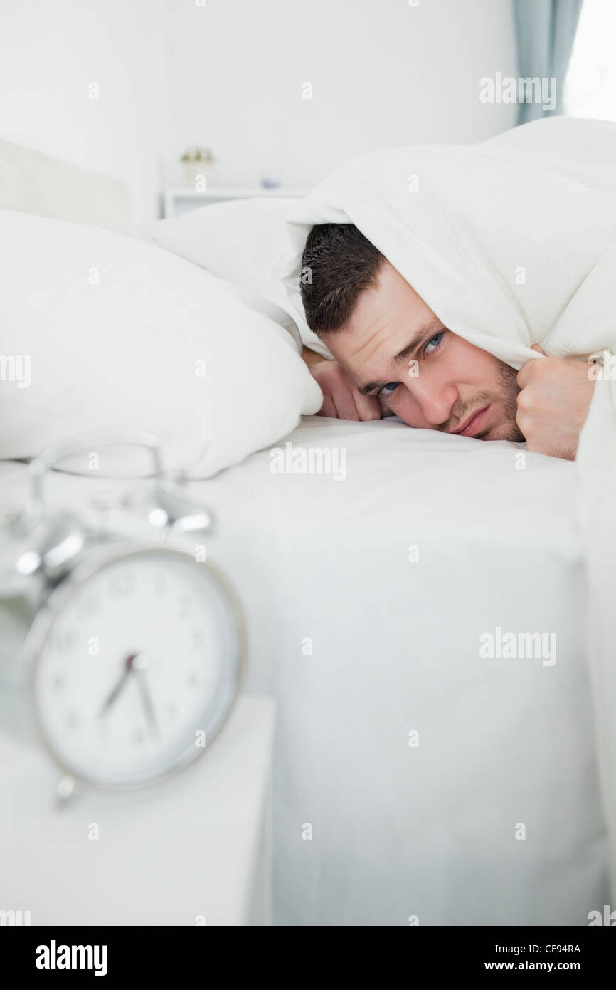 Portrait of a man covering his ears while his alarm clock is ringing