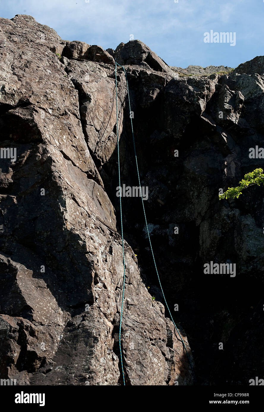 A climbers top rope hangs down a dolerite rock cliff in the sun at Auchinstarry Quarry, Scotland Stock Photo