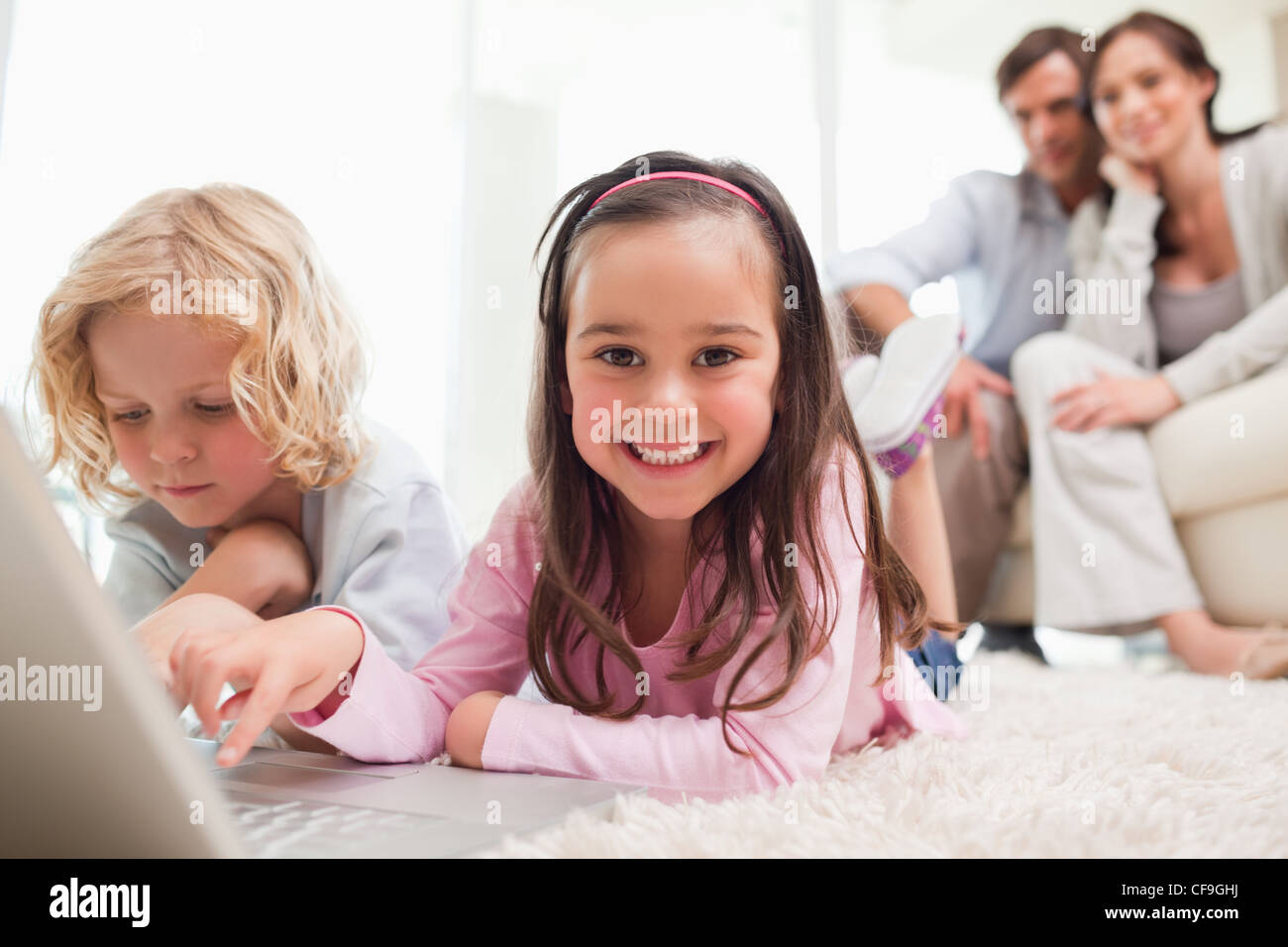 Siblings using a laptop while their parents are in the background Stock Photo