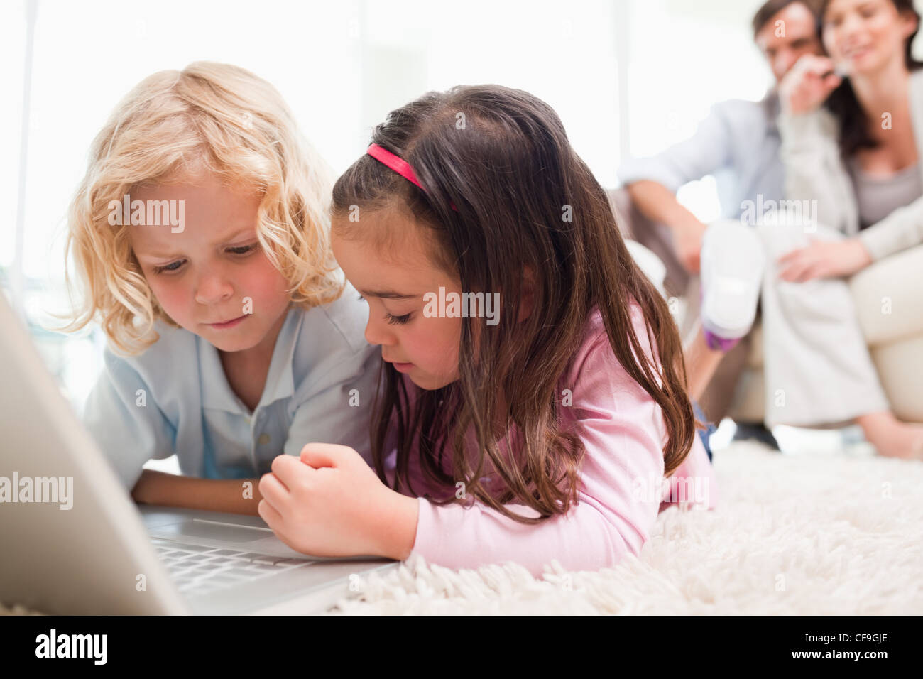 Siblings using a notebook while their parents are in the background Stock Photo