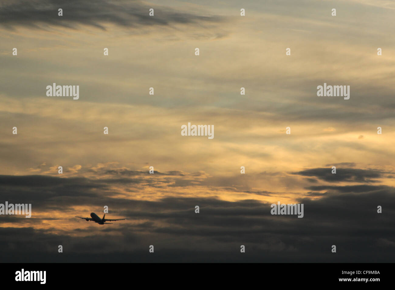 Silhouette of a plane flying away in the cloudy dusk sky Stock Photo