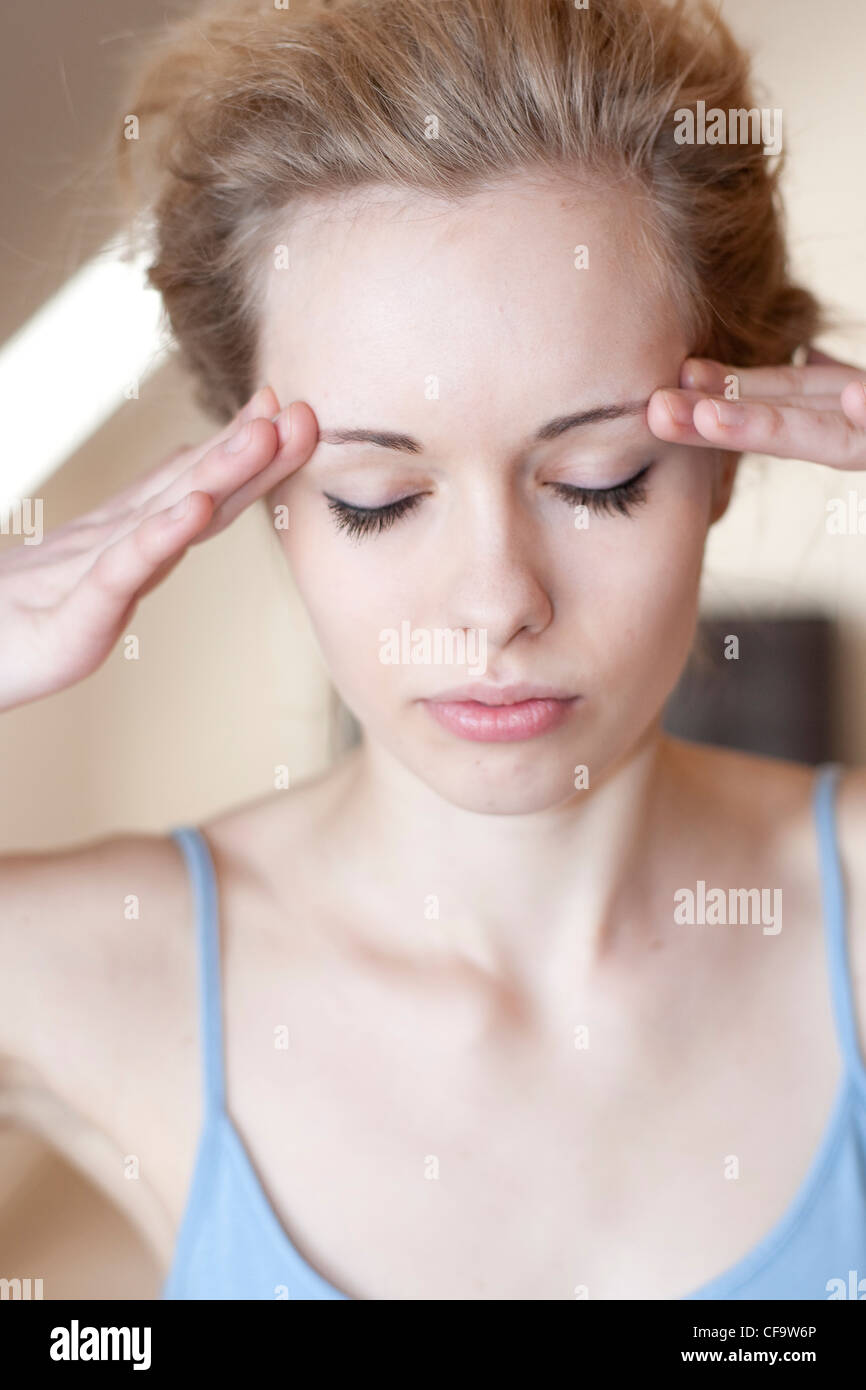 Female With Fair Hair Off Her Face Wearing A Blue Camisole Fingers On Temples Unsmiling With