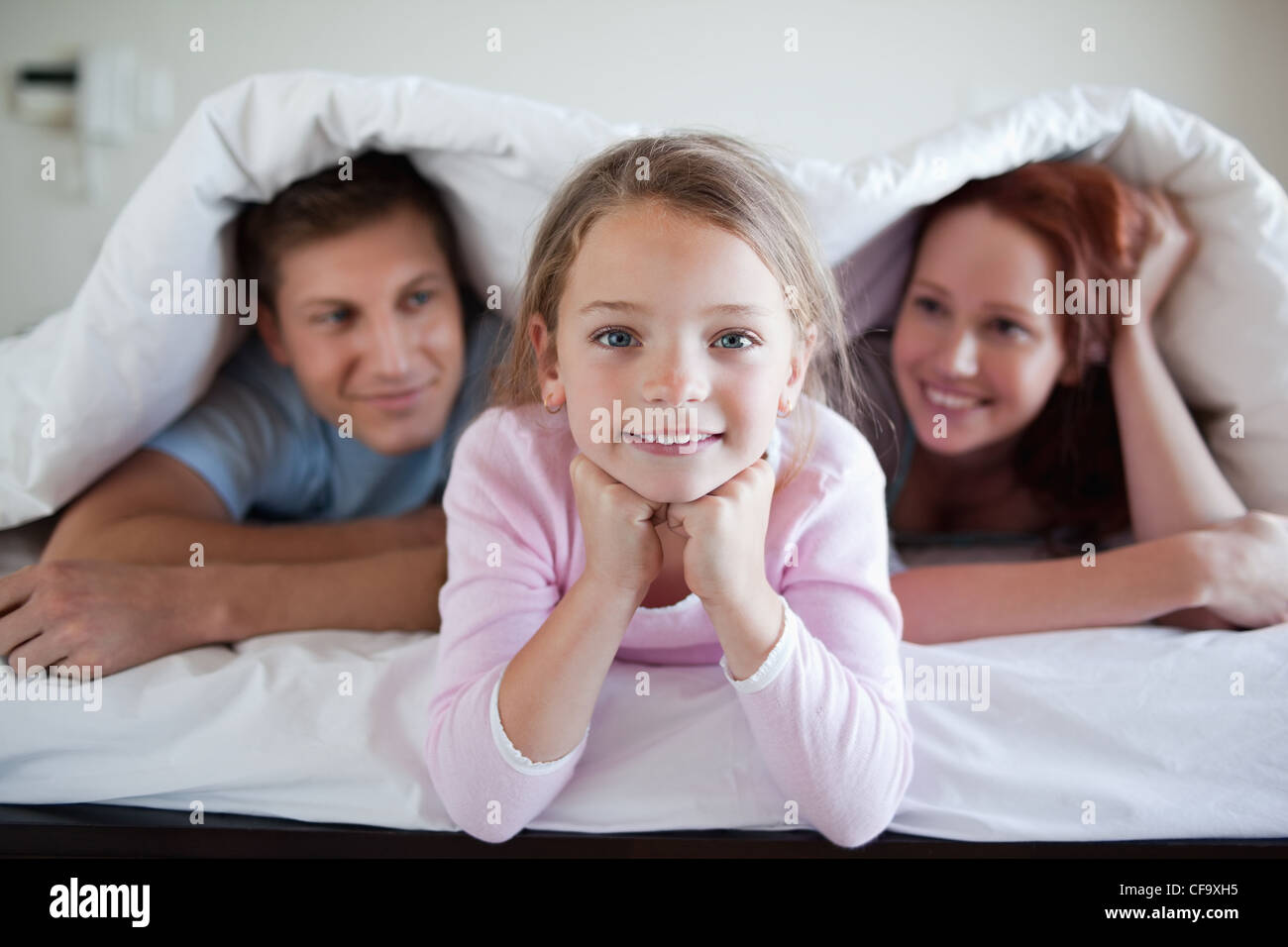 Cheerful girl under bed cover with parents Stock Photo Alamy