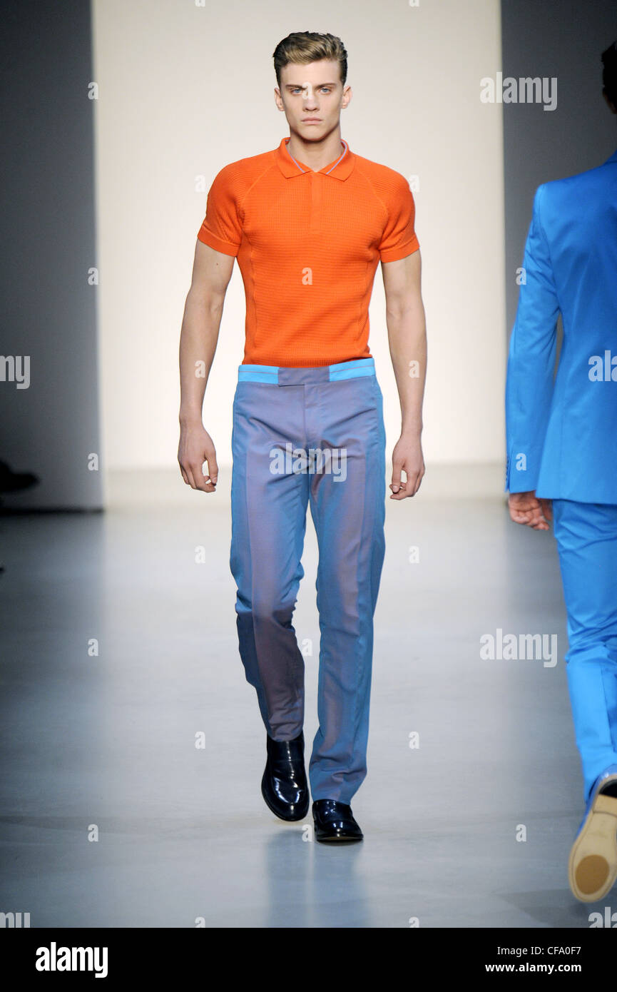 Calvin Klein Milan Ready to Wear Spring Summer Male wearing orange polo shirt and blue trousers Stock Photo