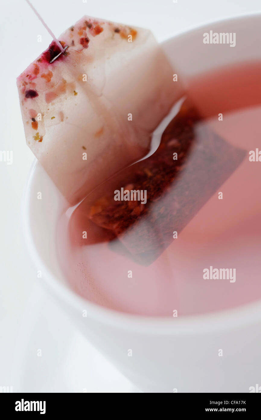 A close up of a white cup and saucer filled with a pink fruit tea with