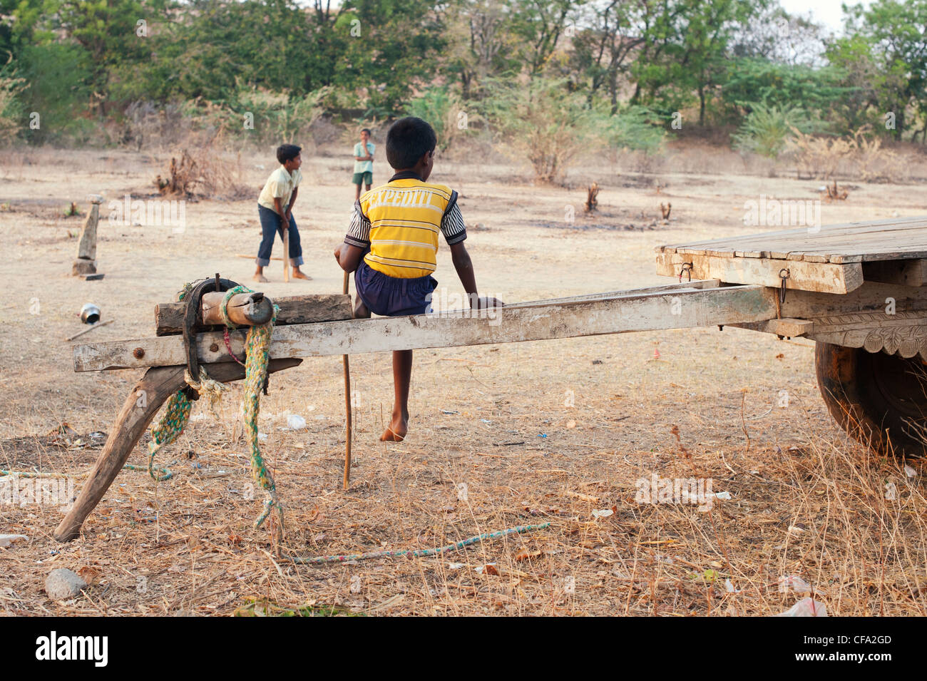 Indian boy watching friends playing cricket in the dry indian countryside. Andhra Pradesh, India Stock Photo