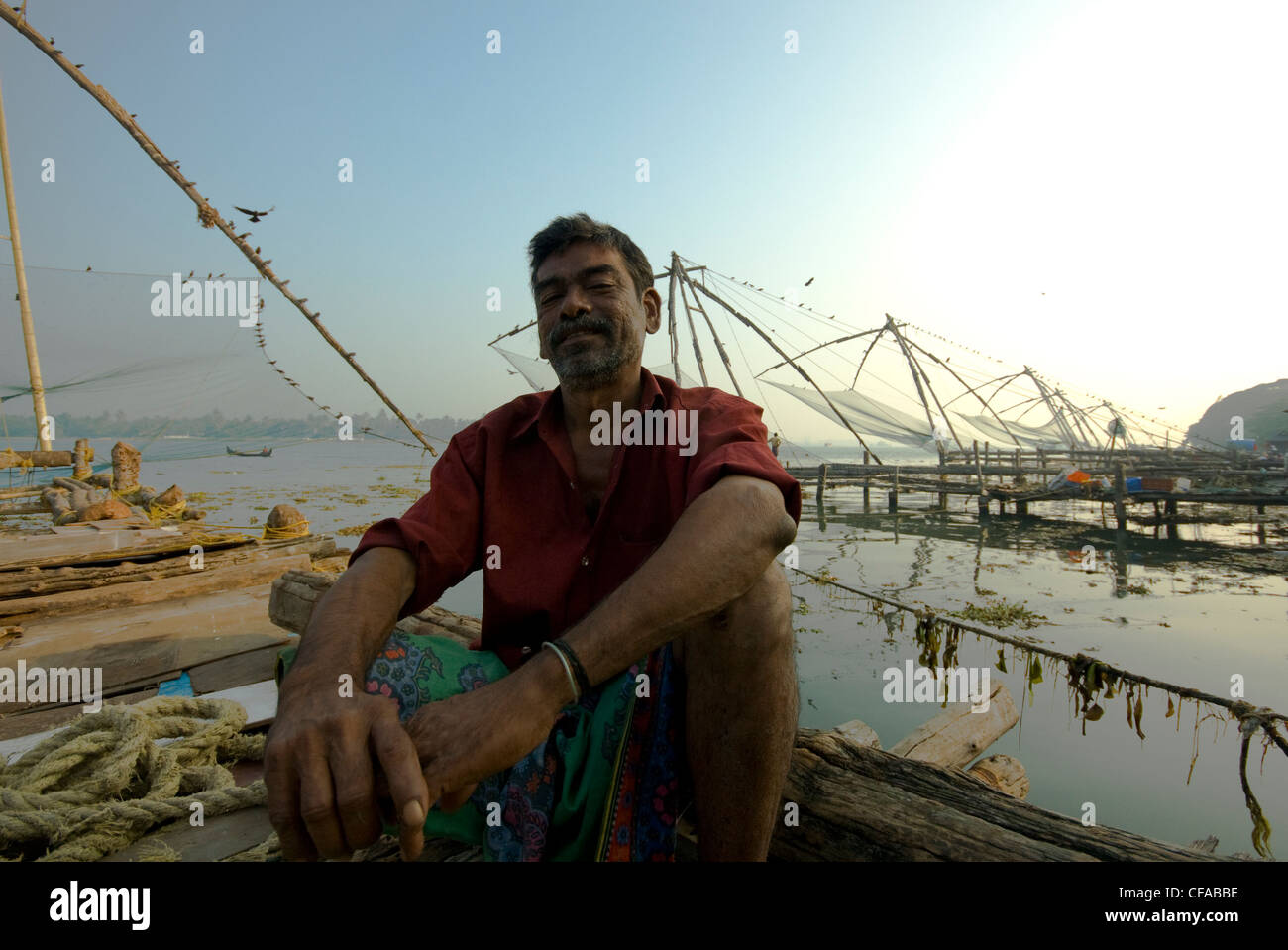 Indian fisherman Babu sits on his Chinese fishing net Stock Photo