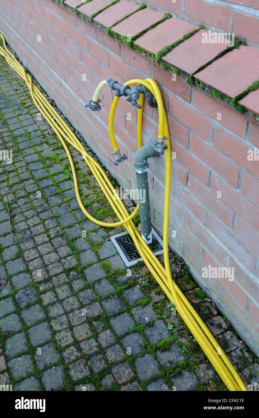 Garden hose tap outlet on house wall with yellow hosepipe, Stock Photo