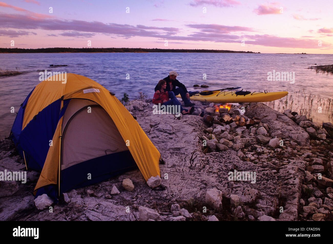 Campers enjoy a campfire next to their kayak, at sunset, on the shore of Lake Huron, Ontario, Canada. Stock Photo