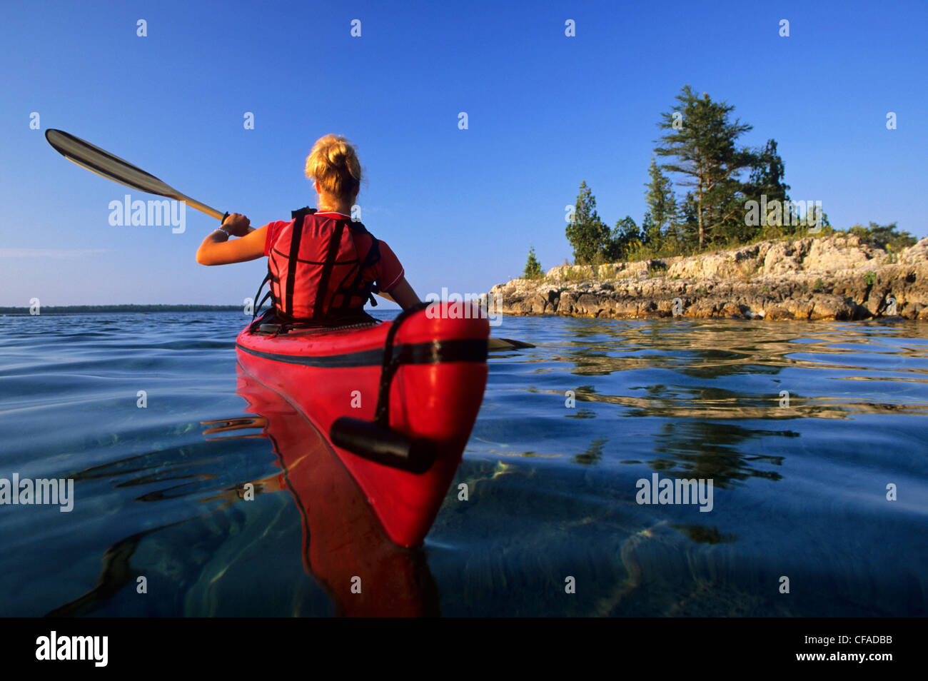 A young woman paddles her kayak at sunset along the Lake Huron shoreline, Fathom Five National Marine Park, Ontario, Canada. Stock Photo