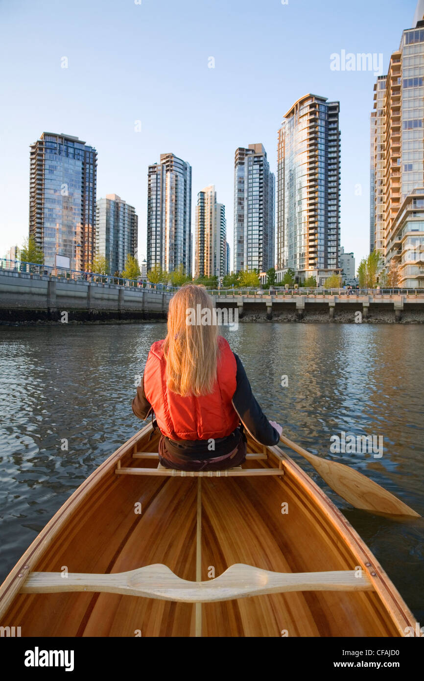 Girl paddling canoe across from downtown condominiums, False Creek