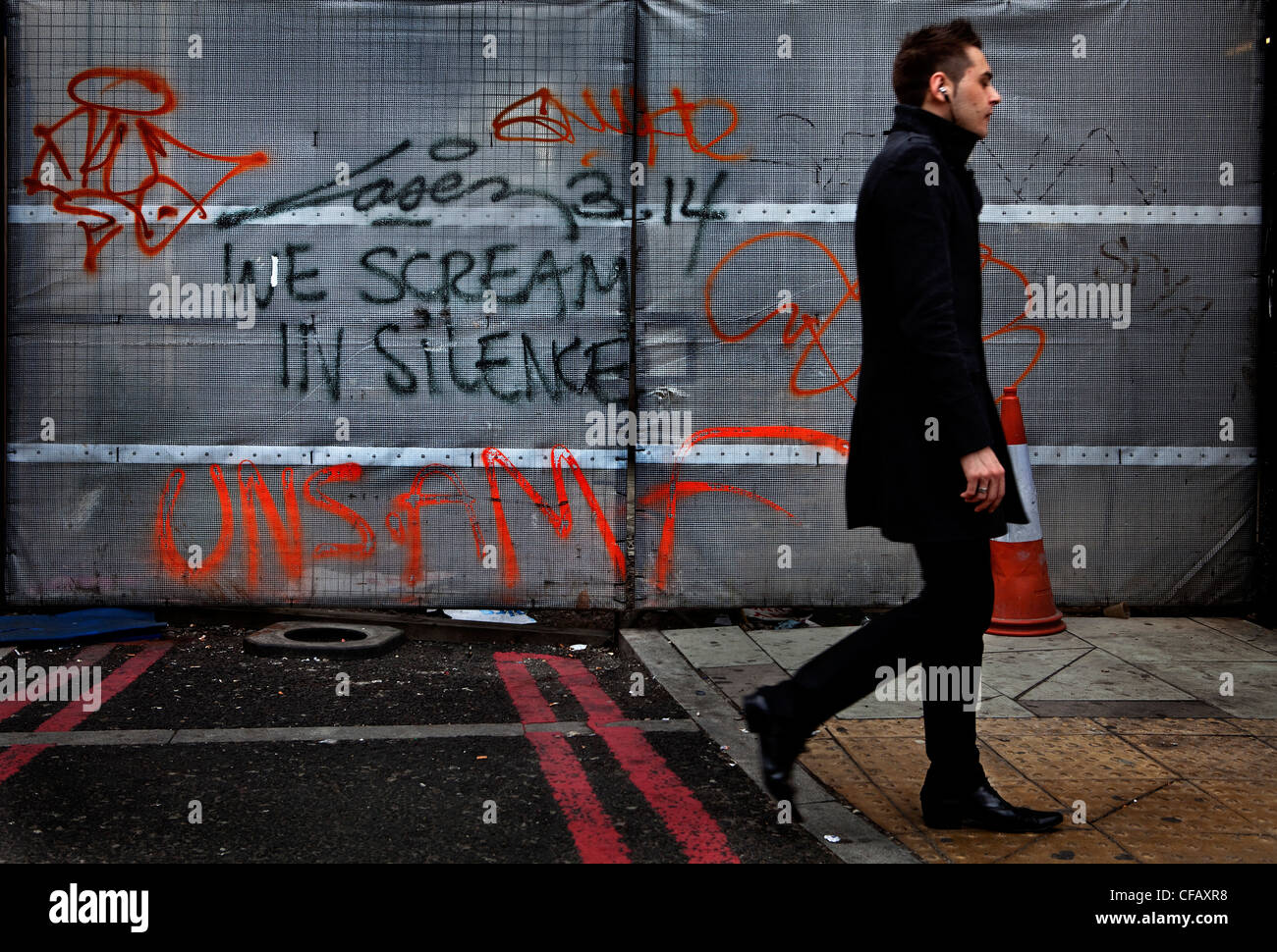 Street graffiti with young man walking past the statement 'We scream in silence', Whitechapel, London. Stock Photo