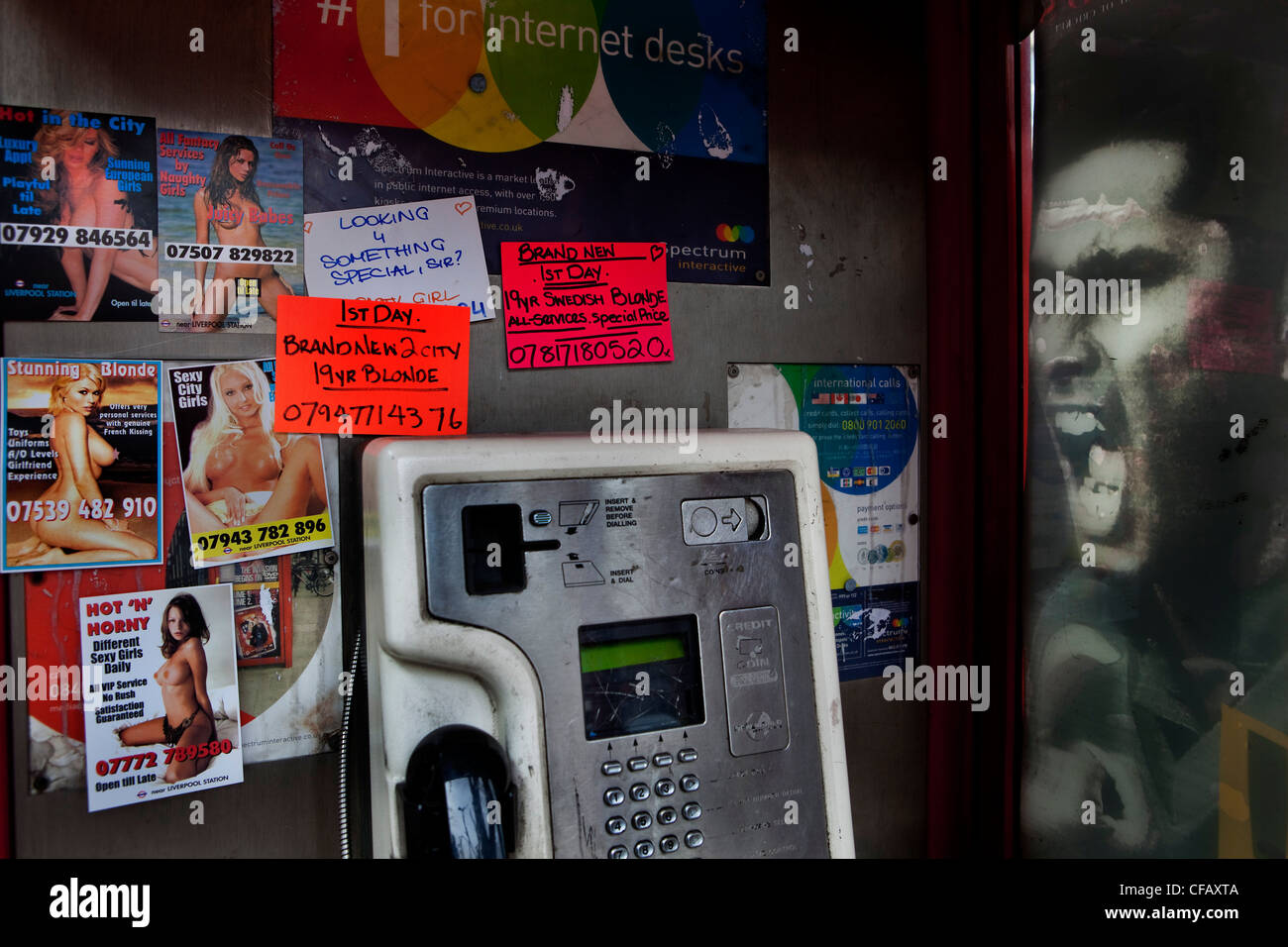 Telephone booth with call girl post cards and face of Mohamed Ali on advert outside. Stock Photo