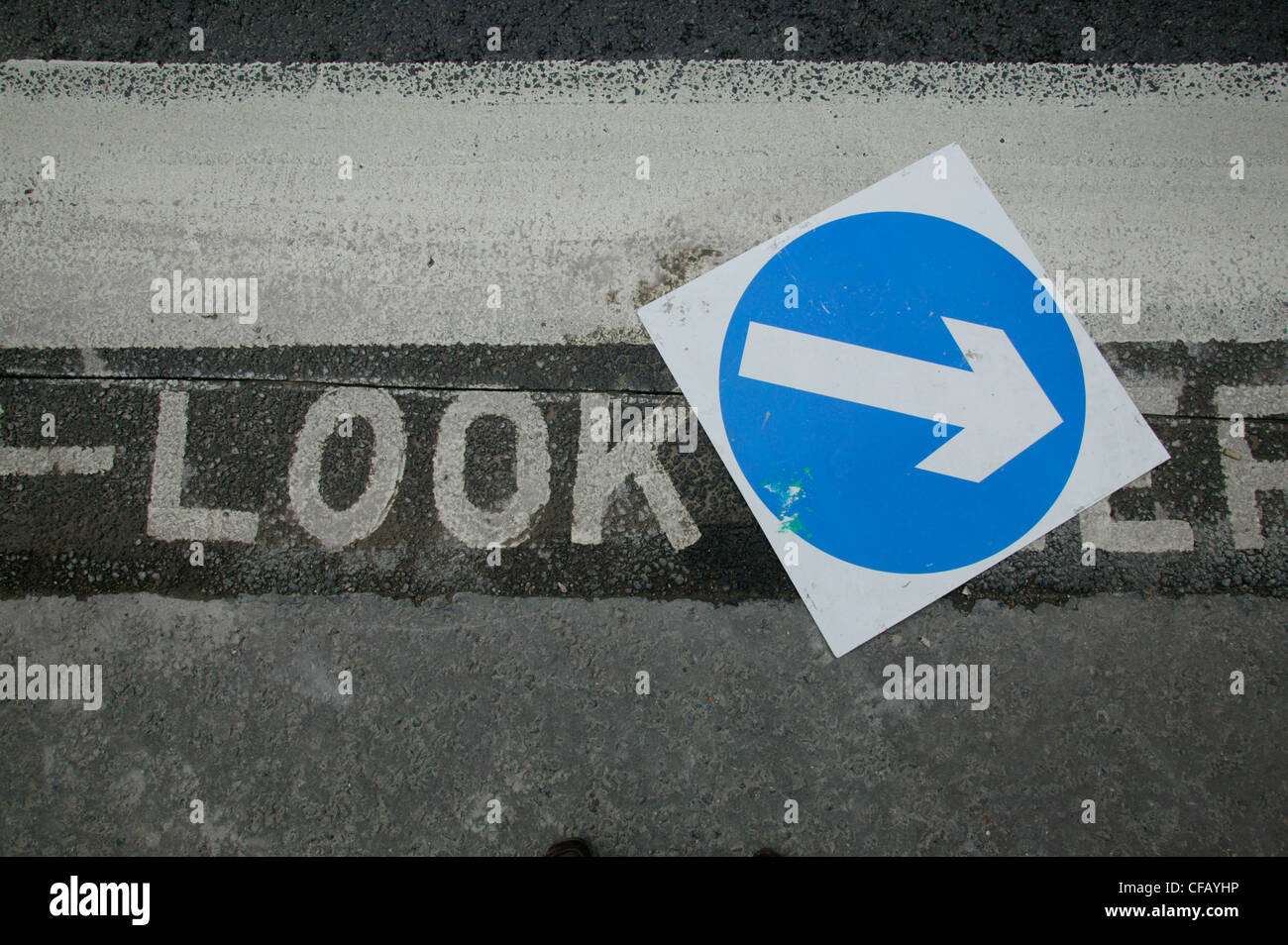 A blue sign on the road surface covering a 'look left' instruction painted on the road, London. Stock Photo