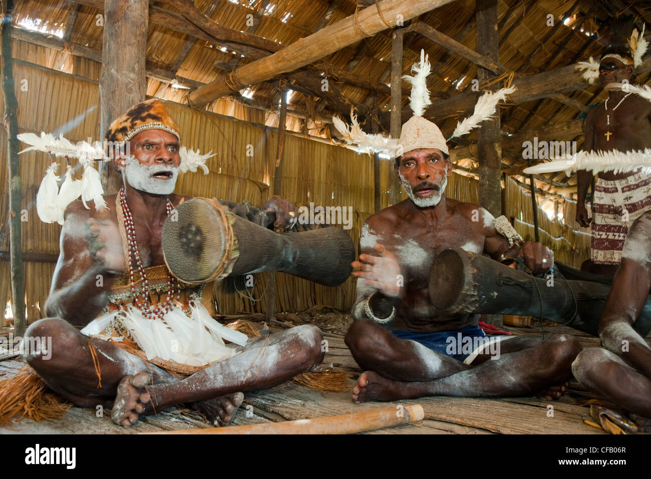 Men from the Asmat Tribe playing drums and singing, Agats village, New Guinea, Indonesia. Stock Photo