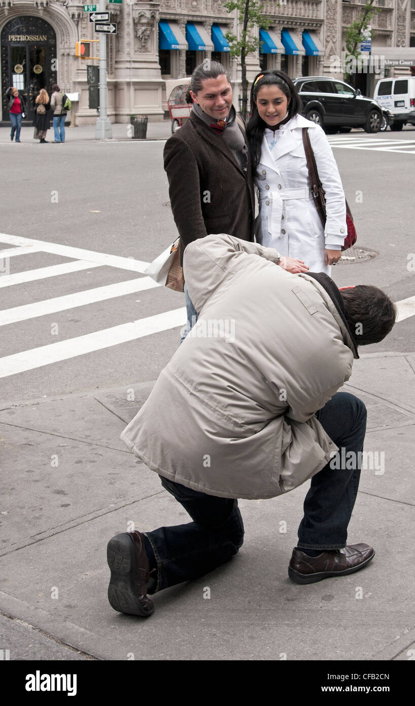 A photographer gets down on one knee to get the proper angle to capture a couple's image in New York City. Stock Photo