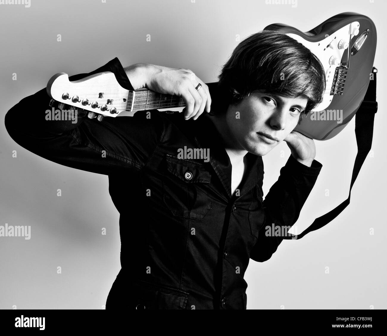 Half length studio black and white portrait of man wearing dark shirt holding electric guitar behind his head on his shoulders Stock Photo