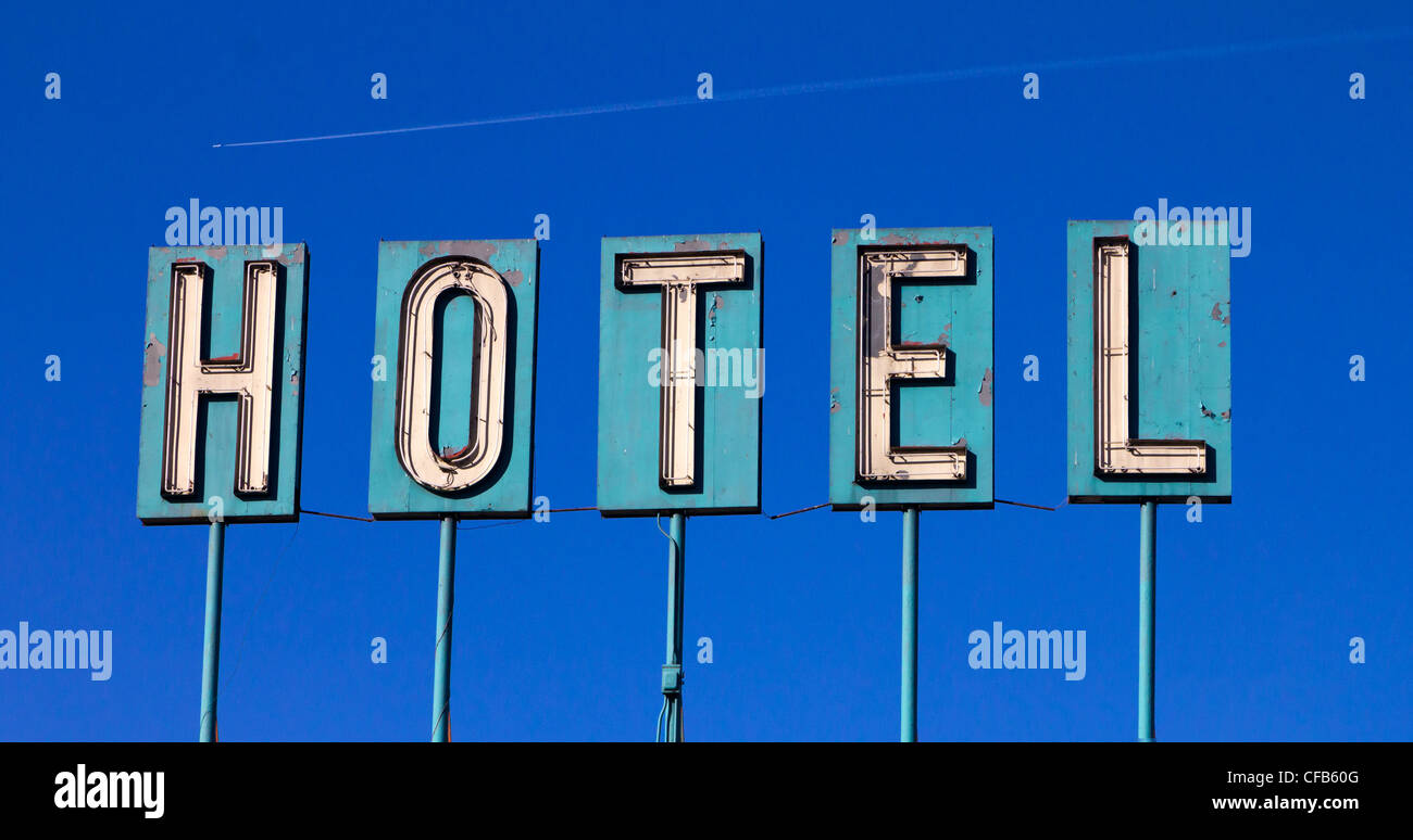 Grungy old hotel sign isloated on a blue sky background with an airplane flying in the distance Stock Photo