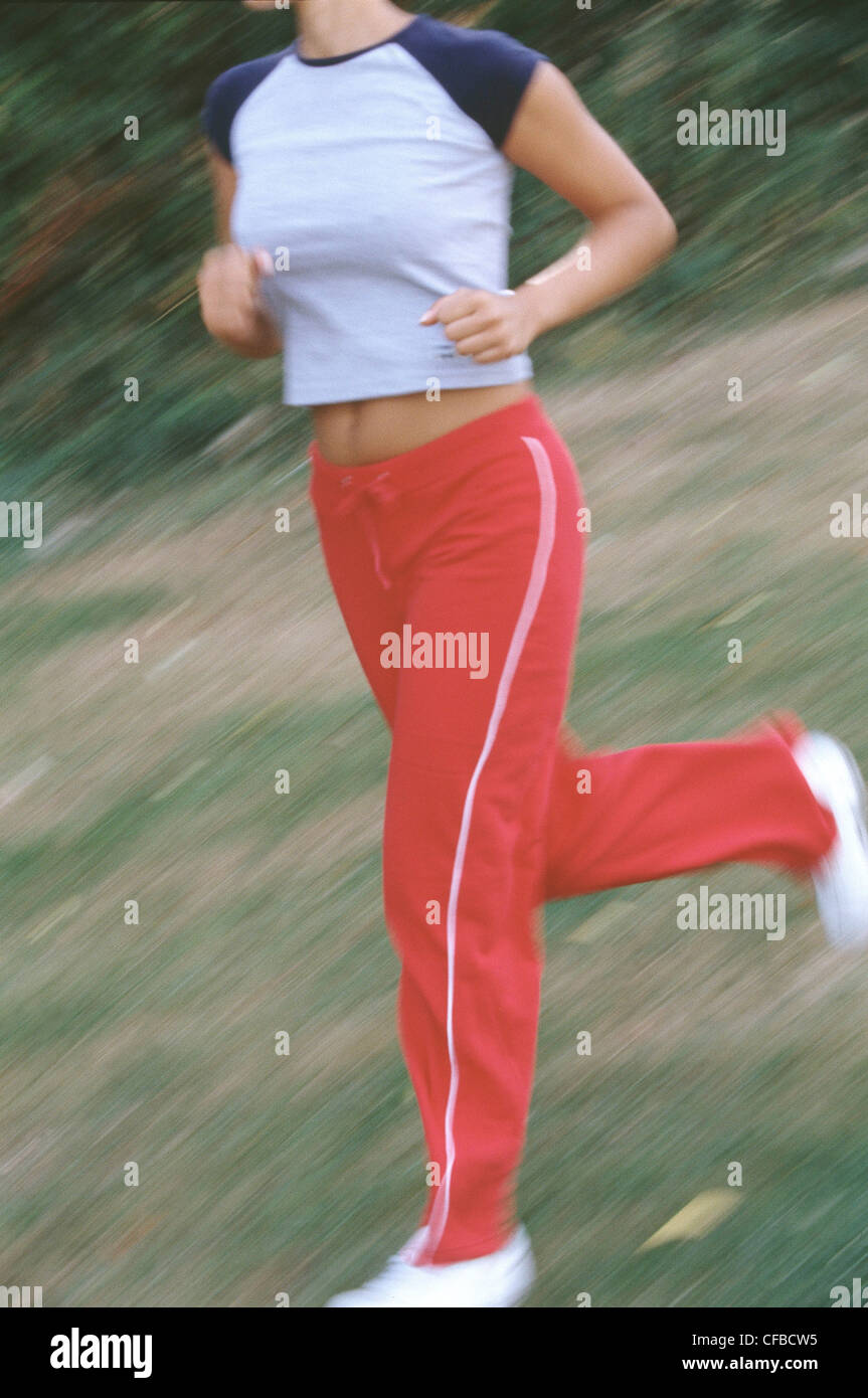 Cropped blurred semi profile of female wearing cropped grey t shirt navy blue sleeves red tracksuit bottoms and white trainers Stock Photo