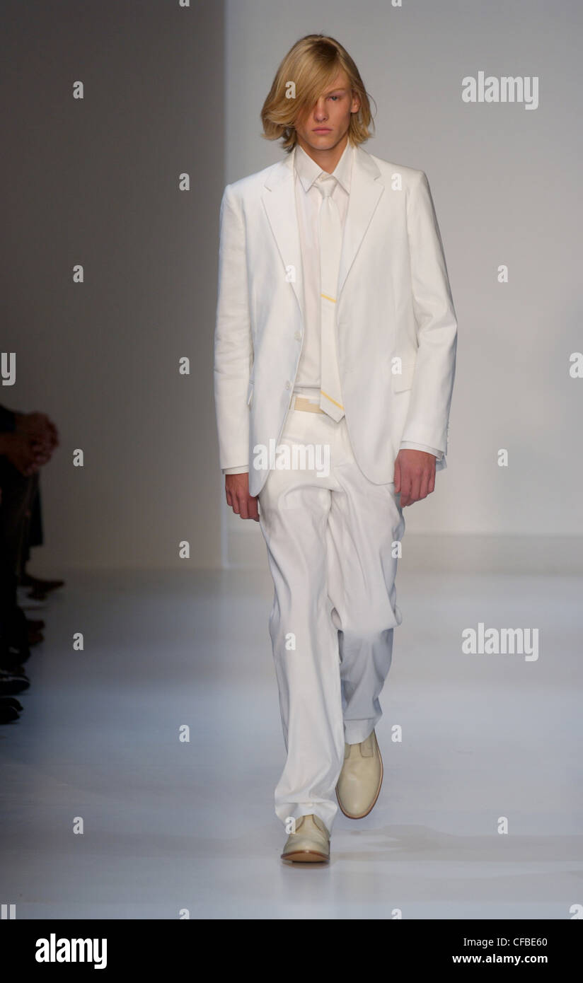 Calvin Klein Menswear Ready to Wear Spring Summer Model long blond hair wearing white jacket, white shirt, white tie thin Stock Photo