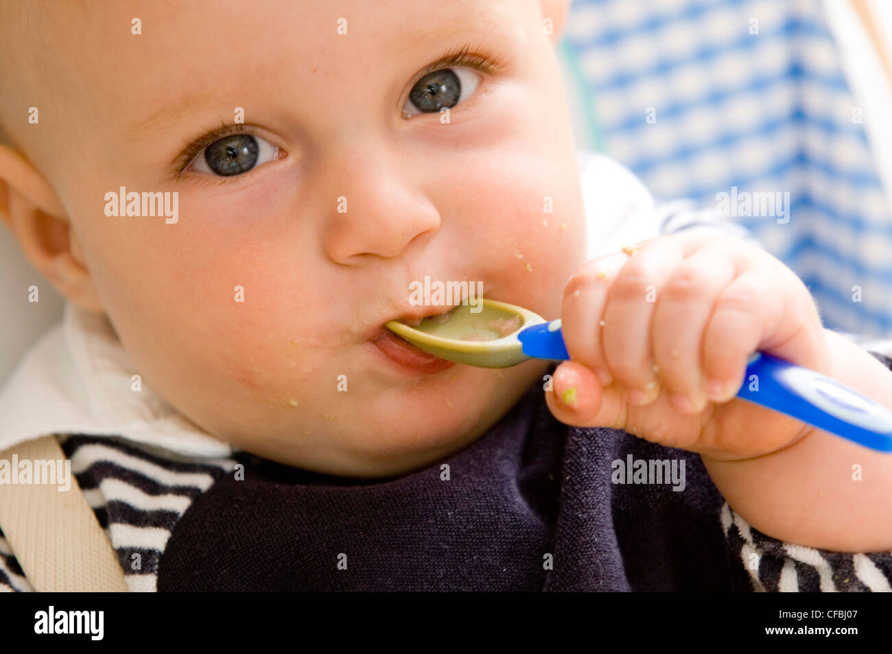 Cropped image of blonde male child aged months wearing a black and white stripey top and a black bib feeding himself baby food Stock Photo
