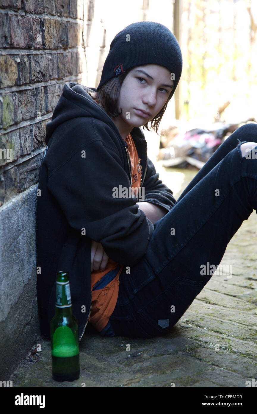 Teenage boy long dark hair wearing black beanie hat, hooded top, orange t  shirt and black jeans sitting on ground against Stock Photo - Alamy